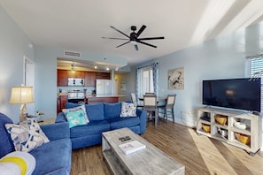A living room with a sofa, coffee table, TV stand, and a ceiling fan. - Inviting lakefront condo w/ amazing views, 5 pools, on-site golf, gym & hot tub (Panama City Beach)