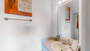 Een badkamer met een wastafel, spiegel en handdoekrek. Er is een bord op de muur en een handdoek hangt aan het rek.