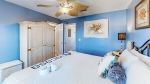 Een slaapkamer met een bed, een plafondventilator, een kledingkast, een deur en een ingelijste foto aan de muur.
