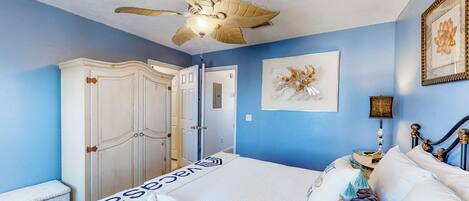 A bedroom with a bed, a ceiling fan, a wardrobe, a door, and a framed picture on the wall.