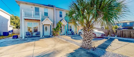 A two-story house with a balcony, a patio with outdoor furniture, and a palm tree.
