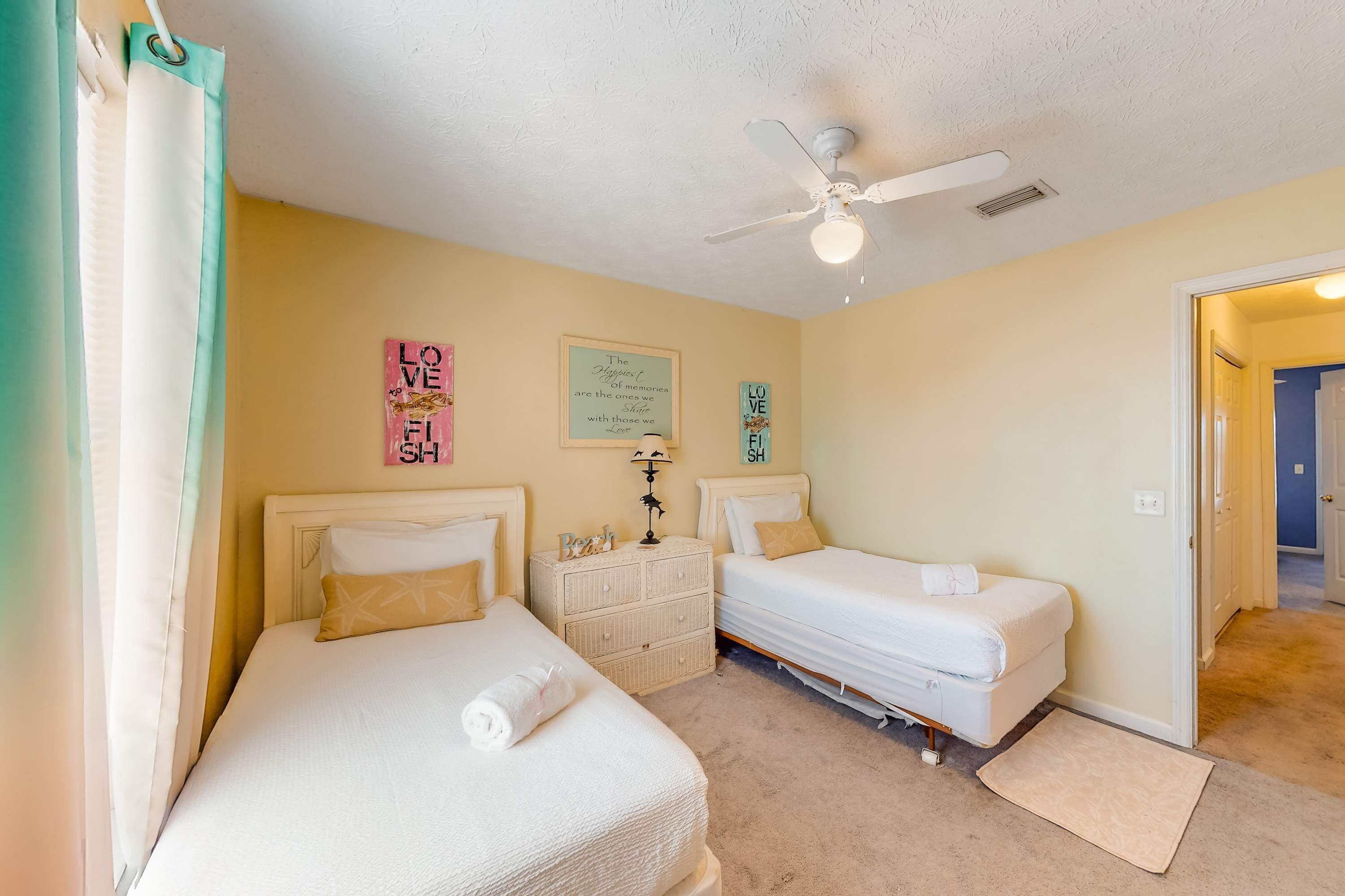 A bedroom with two beds, a ceiling fan, and a door leading to another room.