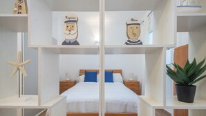 A hotel room with a bed, two nightstands, a starfish decoration, a potted plant, and two wooden figures labeled "Kapitan" and "Moin". - Estudio en primera línea de playa (Las Palmas de Gran Canaria)