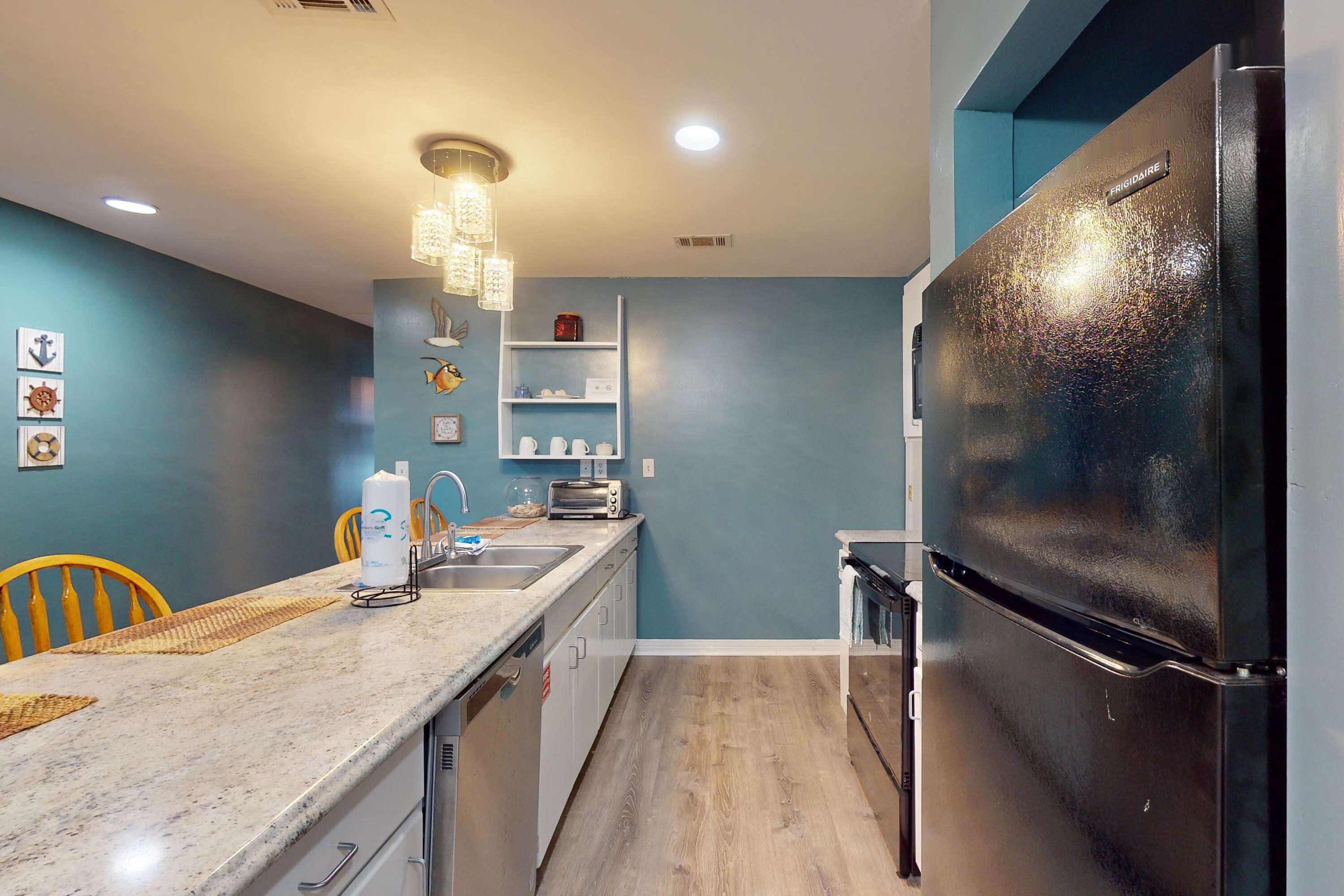 A modern kitchen with a black refrigerator, a marble countertop, and a wooden floor.