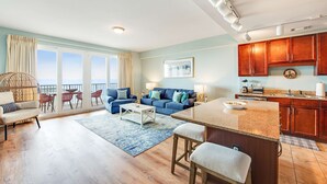 A spacious living room with a blue sofa, a coffee table, and a dining area with a kitchen in the background. - 14th-Floor Condo w/Gulf Views, W/D, Shared Pools, Hot Tubs, WiFi, & Central A/C (Panama City Beach)