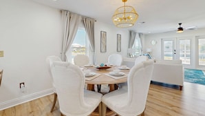 A dining area with a round table, white chairs, a chandelier, and a view of the ocean. - Nautical home in beach community with Water views close to beach access (Navarre)