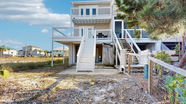 A two-story beachfront house with a balcony, a staircase leading to the upper level, and a fenced outdoor area. - Nautical home in beach community with Water views close to beach access (Navarre)