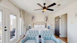 A bedroom with a bed, two armchairs, a ceiling fan, and a view of the outside. - Nautical home in beach community with Water views close to beach access (Navarre)
