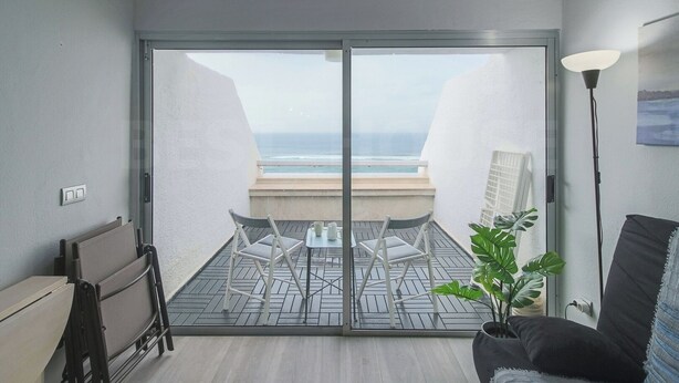 Uma varanda com vista para o oceano, uma mesa com cadeiras e um vaso de planta.