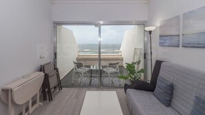 Uma sala de estar moderna com vista para o mar, uma varanda com mesa e cadeiras, e um sofá.
