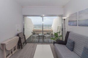 Un moderno salón con vista al mar, un balcón con mesa y sillas, y un sofá.