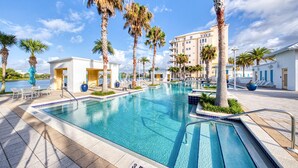 A swimming pool with clear blue water, surrounded by palm trees and a building with balconies. - Sunset-view dog-friendly condo w balcony overlooking water, beach access, pool & hot tub (Panama City Beach)