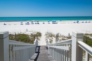 A wooden staircase leading to a beach with white sand and blue umbrellas. - Sunset-view dog-friendly condo w balcony overlooking water, beach access, pool & hot tub (Panama City Beach)