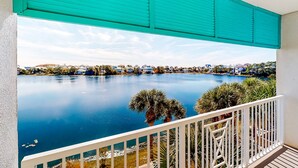A balcony with a view of a calm lake, surrounded by palm trees and houses. - Sunset-view dog-friendly condo w balcony overlooking water, beach access, pool & hot tub (Panama City Beach)