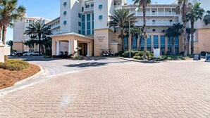 A hotel with a central entrance, palm trees, and a clear sky. - Sunset-view dog-friendly condo w balcony overlooking water, beach access, pool & hot tub (Panama City Beach)