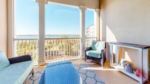 Un balcon avec vue sur la mer, un canapé, un fauteuil et une petite table agrémentée d’objets décoratifs.