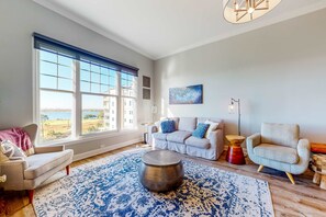 Ein Wohnzimmer mit großem Fenster, einer Couch, einem Couchtisch und einem Sessel.