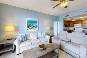 A living room with a sofa, a coffee table, and a kitchen area with cabinets and a microwave. - Beach home with balcony Gulf views & shared pool/hot tub (Panama City Beach)