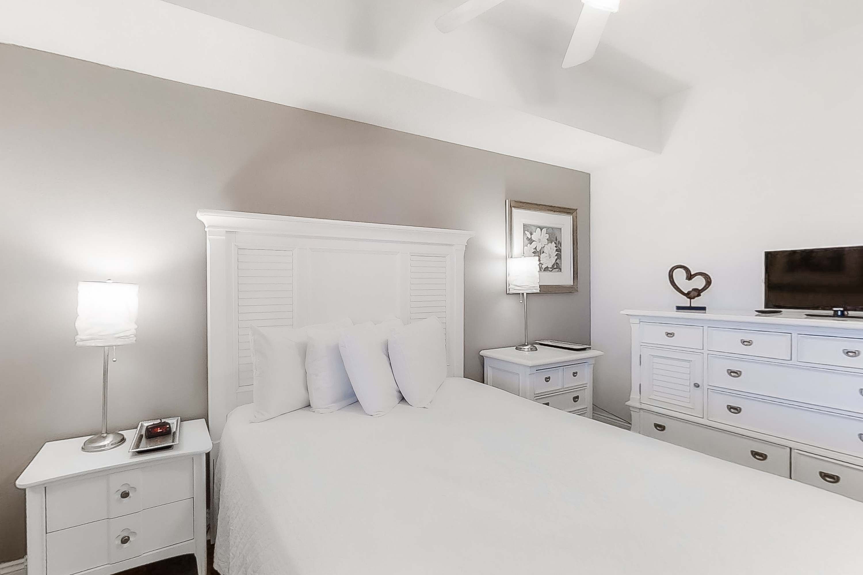 Un dormitorio con cama, mesitas de noche, cómoda, lámpara y televisor.
