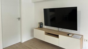 A room with a flat-screen TV mounted on the wall, a wooden cabinet below, and a white door. - Las Tabaibas beach house (San Bartolomé de Tirajana)