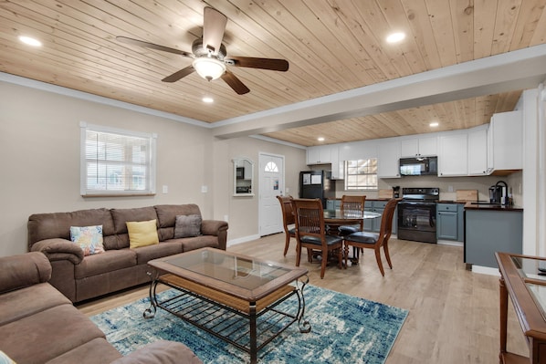 A spacious living area with a ceiling fan, a dining table with chairs, a kitchen with cabinets and appliances, and a large window with blinds. - New listing! Dog-friendly beach escape with a full kitchen & furnished back patio (Panama City Beach)