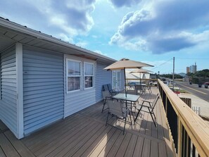 En terrasse med udendørs møbler, et overdækket område med parasoller og udsigt til gaden og bygningerne i baggrunden.