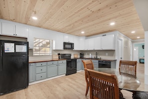 A modern kitchen with white cabinets, a black refrigerator, a microwave, and a dining area with a glass table and wooden chairs. - New listing! Dog-friendly beach escape with a full kitchen & furnished back patio (Panama City Beach)
