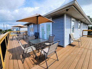 A deck with outdoor furniture, a covered table, and a house with blue siding. - New listing! Dog-friendly beach escape with a full kitchen & furnished back patio (Panama City Beach)
