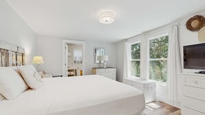Ein Schlafzimmer mit einem großen Bett, einem Schminktisch, einem Fernseher und einem Fenster mit Vorhängen.