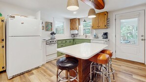 Eine moderne Küche mit einem weißen Kühlschrank, grünen Schränken, einer weißen Kücheninsel mit Hockern und Holzbalkendecke.