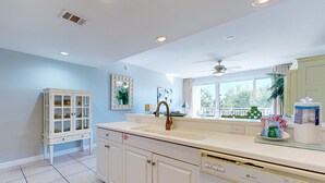 Una cocina moderna con armarios blancos, un lavamanos doble y una ventana con vistas a palmeras.