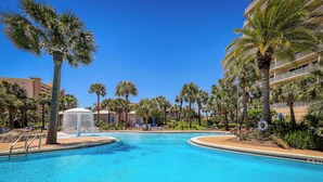 Una piscina con palmeras y una fuente de agua, rodeada por un edificio con balcones.