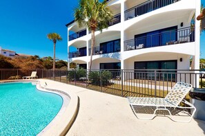 A multi-story hotel with a swimming pool, lounge chairs, and palm trees. - Beachfront Corner Condo with Free WiFi, Stunning Gulf View, & a Shared Pool (Santa Rosa Beach)