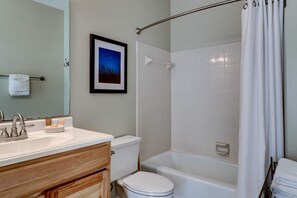 A bathroom with a white sink, wooden vanity, a framed picture on the wall, a white toilet, and a bathtub with a shower curtain. - Beachfront Corner Condo with Free WiFi, Stunning Gulf View, & a Shared Pool (Santa Rosa Beach)