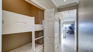 Een slaapkamer met stapelbedden, een gang die leidt naar een keuken en een eettafel.