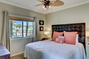 A bedroom with a large bed, a ceiling fan, a window with curtains, and a view of buildings outside. - Beachfront Corner Condo with Free WiFi, Stunning Gulf View, & a Shared Pool (Santa Rosa Beach)
