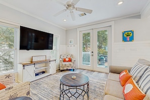 A living room with a ceiling fan, a flat-screen TV, a sofa, and a chair. - Beautiful Home S of 30a, By Gulf, Beaches, Pool, & Dune Lakes (Santa Rosa Beach)