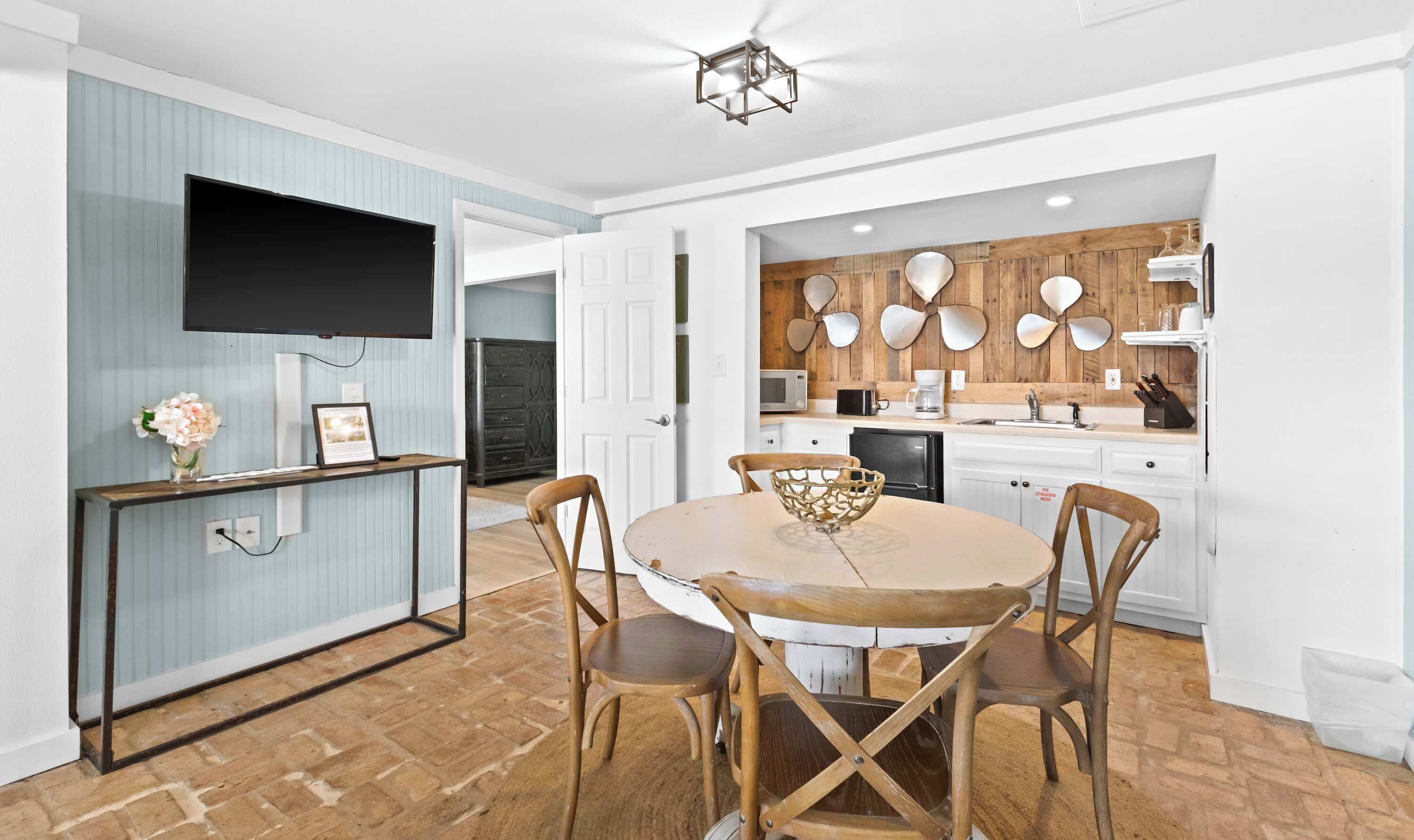 Een moderne keuken met houten details, een eethoek met een ronde tafel en stoelen, en een aan de muur bevestigde televisie.