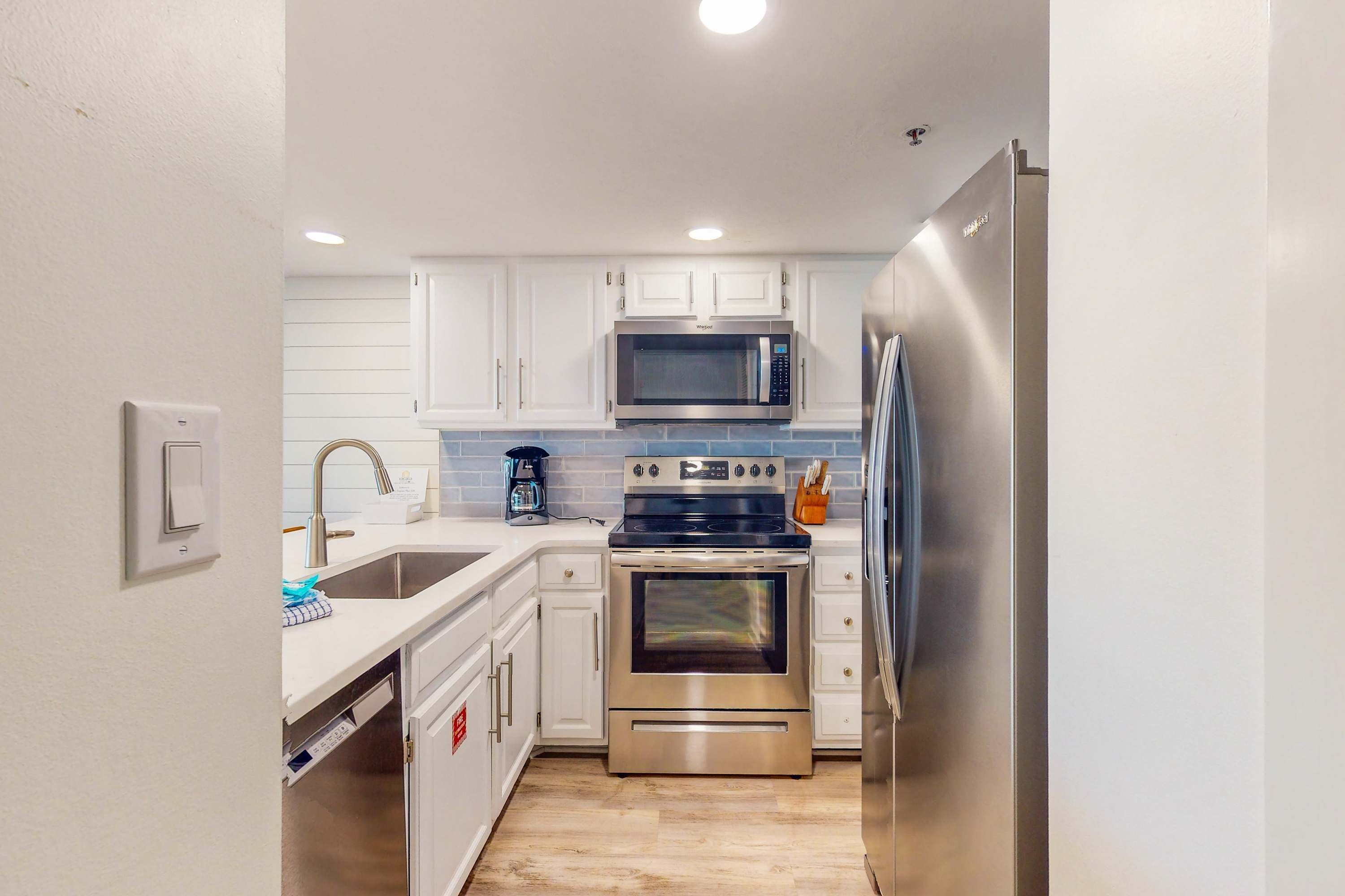 A compact kitchen with white cabinets, a stainless steel refrigerator, a microwave, an oven, and a sink.