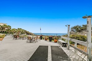 Une terrasse en bois avec des meubles d’extérieur, des plantes en pot et une vue sur l’océan.