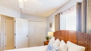Una camera da letto con un letto, un comodino, una lampada, una finestra con tende e una porta.