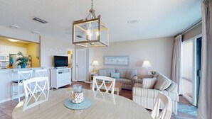 A modern living room with a dining area, a kitchen in the background, and a large window with curtains. - Gorgeous beachfront condo with shared pool, hot tub and beach access (Panama City Beach)