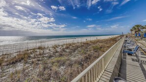 A beach view with a wooden boardwalk, beach chairs, and umbrellas. - Gorgeous beachfront condo with shared pool, hot tub and beach access (Panama City Beach)