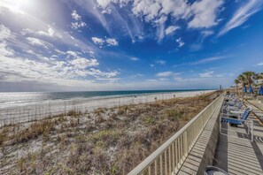 A beach view with a wooden boardwalk, beach chairs, and umbrellas. - Gorgeous beachfront condo with shared pool, hot tub and beach access (Panama City Beach)