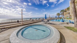 A pool area with a view of the ocean, a palm tree, and a building with balconies. - Gorgeous beachfront condo with shared pool, hot tub and beach access (Panama City Beach)