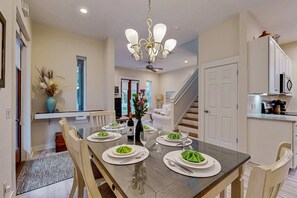 A dining area with a long table set for six, a chandelier, and a view of the living room and kitchen in the background. - Summers Edge, Private Beach, 2 Pools, Bikes (Santa Rosa Beach)