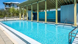 Una piscina con zona cubierta, agua cristalina y un edificio al fondo.