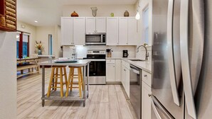 Una cocina moderna con armarios blancos, electrodomésticos de acero inoxidable y un taburete de bar de madera.