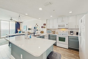 A modern kitchen with white cabinets, a large island, and a ceiling fan. - Modern, Gulf-front condo with pool, hot tub & high-speed WiFi (Panama City Beach)