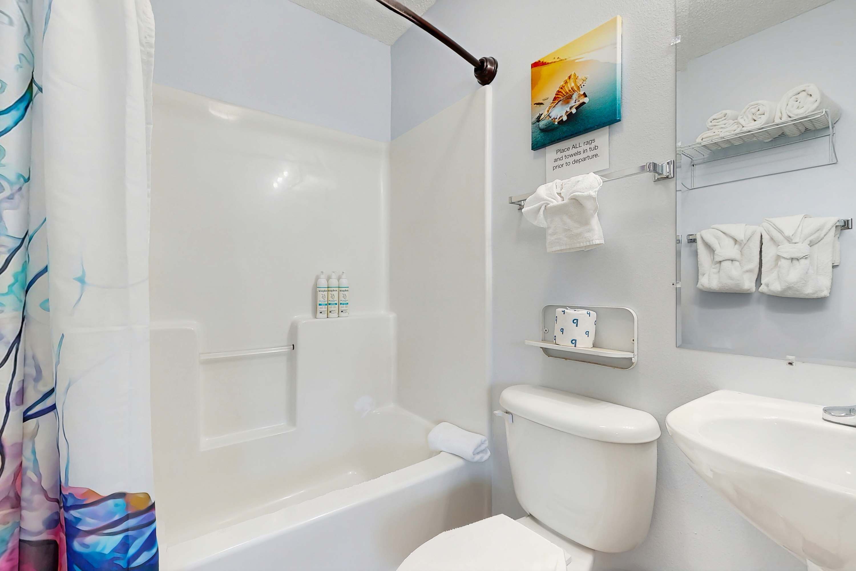 A bathroom with a bathtub, toilet, and sink. There are towels and toiletries on shelves.